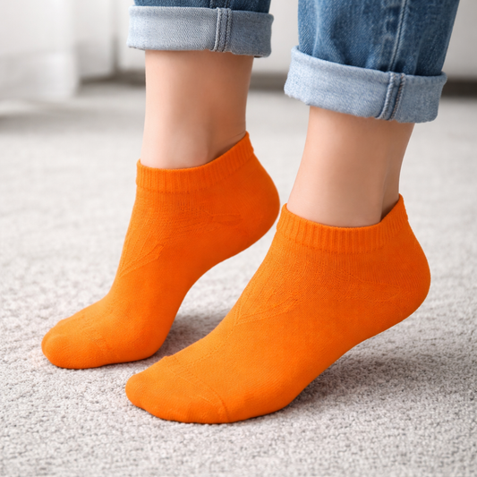 Orange ankle socks worn with rolled-up jeans on a neutral background