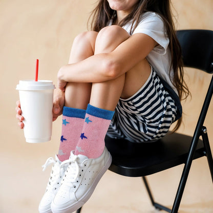 Person sitting on a chair wearing pink socks with blue airplane patterns, holding a white cup with a red straw.