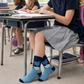 Person wearing blue socks with cat designs sitting at a desk in a classroom.
