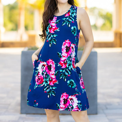 Woman wearing a blue floral dress with pink and green flowers outdoors.