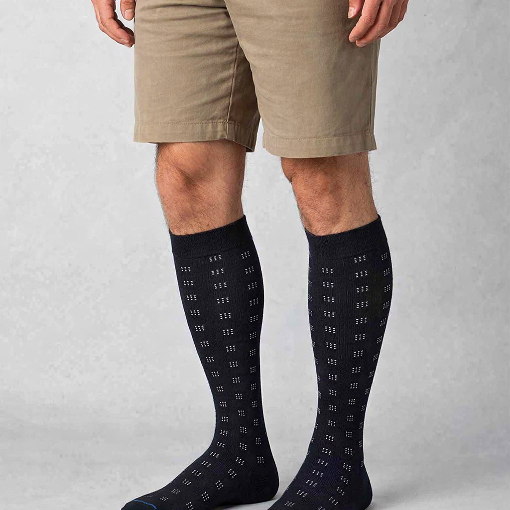 Person wearing black knee-high socks with a subtle pattern on a plain background