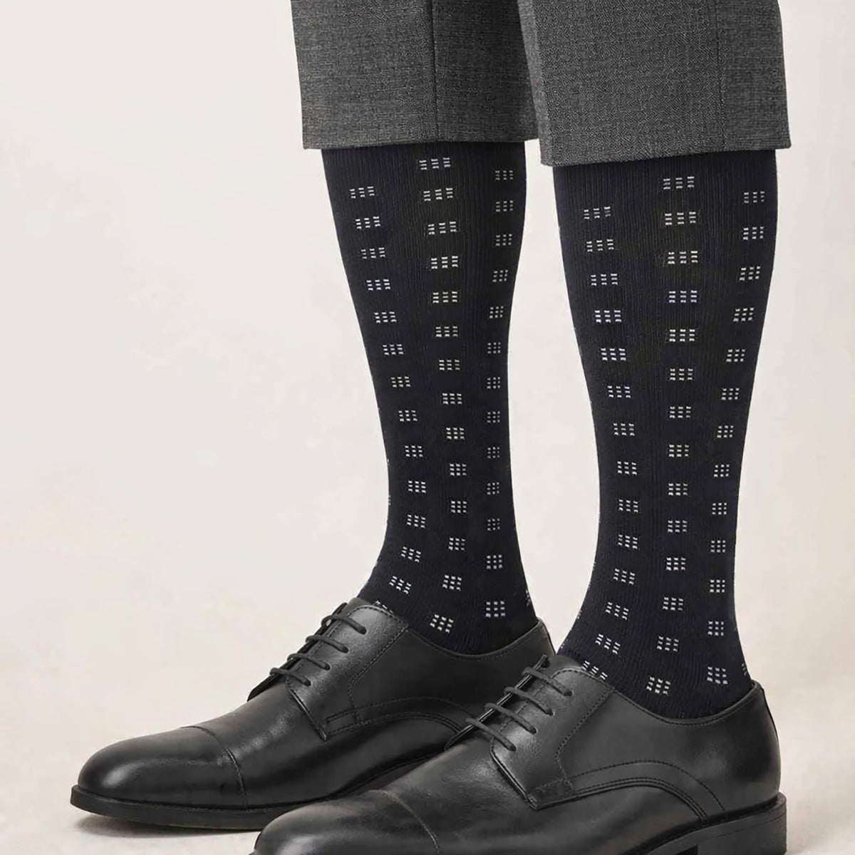 Black dress socks with geometric pattern worn with black shoes and gray pants on a light background