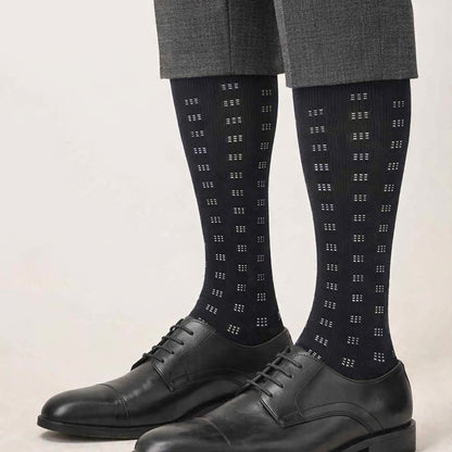Black dress socks with geometric pattern worn with black shoes and gray pants on a light background