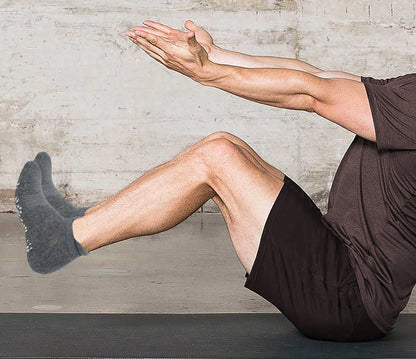 A Person wearing ankle socks performing a yoga pose with one leg raised on a mat against a neutral wall.